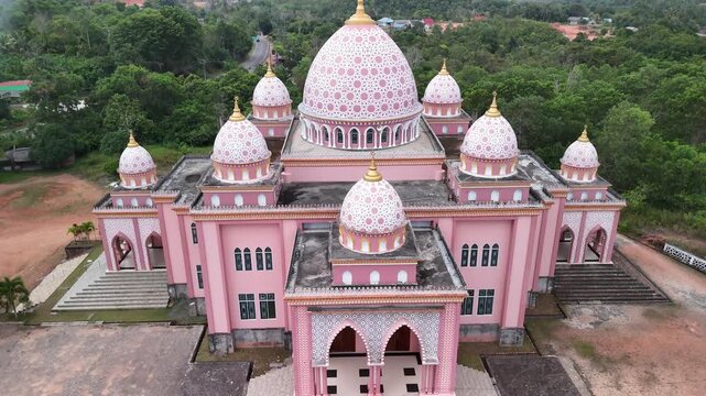 Aerial view of the pink AnNur Mosque in Bintan showcasing its elegant domes and reflection surrounded by lush greenery and tranquil water scenery