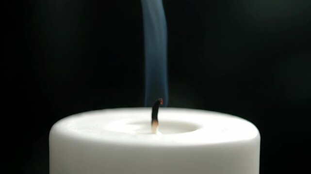 White candle extinguished with smoke creates a somber scene, white candle aftermath features faint wisps rising. Symbolic extinguished candle suggests peaceful moment or spiritual reflection.