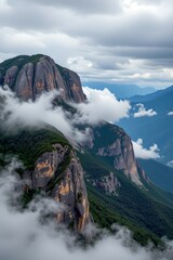 This image depicts a dramatic mountainous landscape shrouded in mist and clouds, The main focus is on towering cliffs with rugged, textured surfaces covered in patches of lush green vegetation