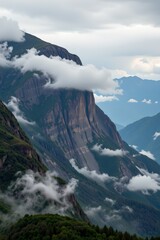 This image depicts a dramatic mountainous landscape shrouded in mist and clouds, The main focus is on towering cliffs with rugged, textured surfaces covered in patches of lush green vegetation