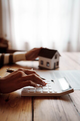 Person signing a real estate contract while holding a small house model, representing home ownership, property investment, and mortgage agreement.