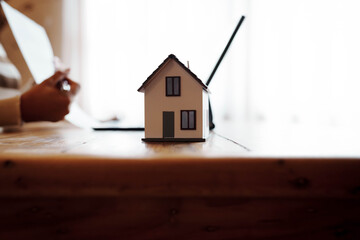 Person signing a real estate contract while holding a small house model, representing home ownership, property investment, and mortgage agreement.