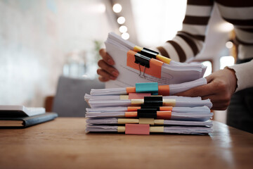 A person organizing stacks of documents with colorful binder clips on a wooden desk in a bright office environment.