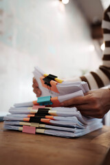 A person organizing stacks of documents with colorful binder clips on a wooden desk in a bright office environment.