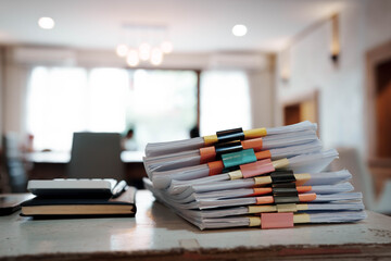 A person organizing stacks of documents with colorful binder clips on a wooden desk in a bright office environment.