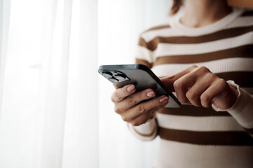 A person using a smartphone with both hands near a bright window, focusing on the screen in a calm, minimalist setting.