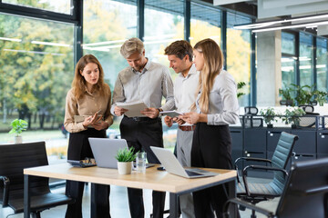 Group of business people standing together and discussing their work and projects, having a team meeting in an office.