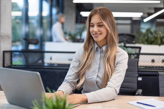 Young business woman is using laptop while sitting in the office, smiling