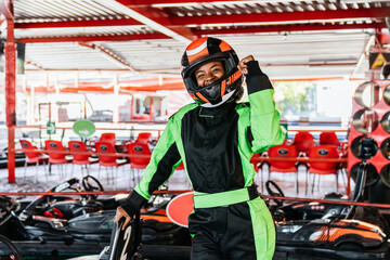 Young african woman in racing helmet raises fist in joyful celebration after winning at an outdoor go kart track championship © Koldo_Studio