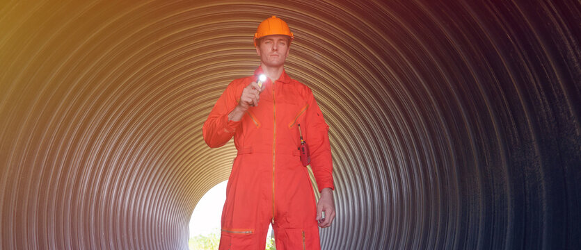A male engineer in an orange suit is inspecting the integrity and safety of a pipeline.