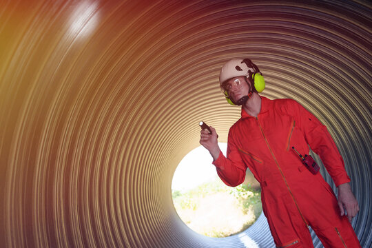 A male engineer in an orange suit is inspecting the integrity and safety of a pipeline.