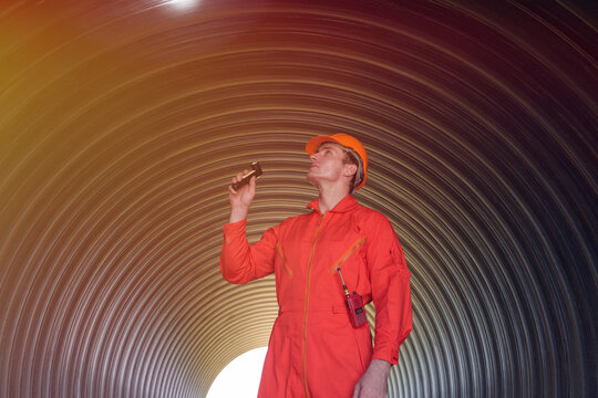 A male engineer in an orange suit is inspecting the integrity and safety of a pipeline.