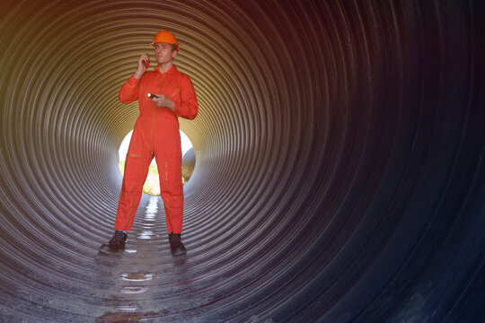 A male engineer in an orange suit is inspecting the integrity and safety of a pipeline.