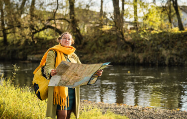 Young woman  traveler with backpack and map searching destination in the forest. 