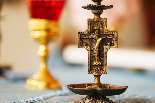 Closeup of vintage Christian golden crucifix with Jesus figure on altar table. Religious symbol of faith, belief, and prayer. Catholic devotion and spirituality with gold chalice background.