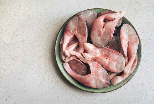 Large, freshly sliced pieces of cleaned silver carp lie on a large green plate on the table. The idea is to prepare a fresh and healthy fish dish.