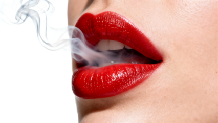 Close-up of a womans red lips exhaling smoke creating a mysterious and alluring visual.