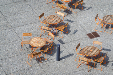 Sunlit café chairs stacked on stone plaza © SILI