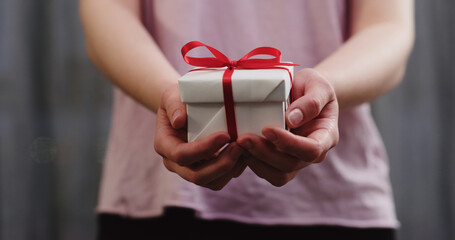young woman stand and show white gift box with red ribbon bow