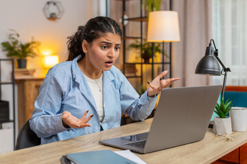 Nervous woman quarrelling laptop call online at home office desk. Emotional Indian girl talking aggressively computer video call. Stressed lady scolding subordinates and closing laptop. Lifestyle.