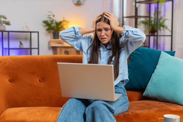Upset woman sitting on sofa at home using laptop having anxiety stress, searching internet can't...
