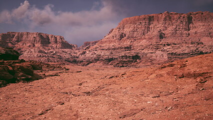 An expansive view of rugged red rock formations under a partly cloudy sky showcases the natural beauty of a remote desert area. The terrain appears dry and vast, evoking a sense of wilderness.