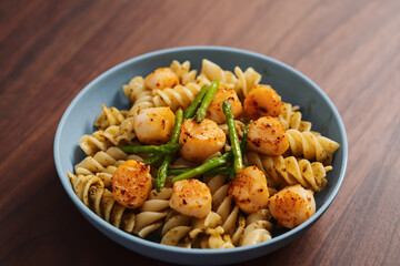 Fusilli pasta with scallops and asparagus in blue bowl on walnut wood surface