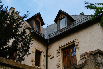 Vintage stone house with two wooden dormer windows and brown doors under blue sky