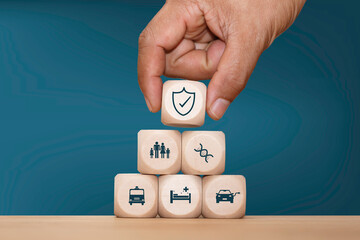Hand stacking wooden blocks with blue insurance icons representing health, family, home, travel, and life protection. Concept for insurance services, financial security, risk management.