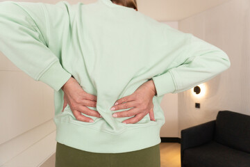 Person feeling back pain and touching lower spine area, showing muscle tension and discomfort. Concept of injury, posture issue and physical wellness in daily life.