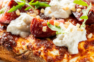 A close-up, top-down view of a gourmet flatbread or pizza with fresh figs, creamy white cheese, toasted pine nuts, and arugula on a crispy, golden crust.