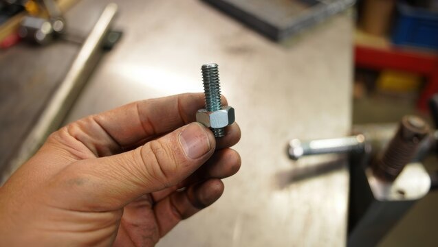 Hand holding a metal bolt and nut, showcasing industrial hardware details