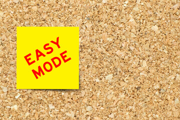 Yellow note paper with word easy mode on cork board background with copy space