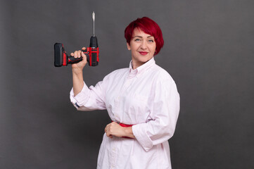 woman holds screwdriver on a neutral gray background, showcasing tool. versatile image provides excellent copy space for advertisements or instructional content. cordless screwdriver in women hands