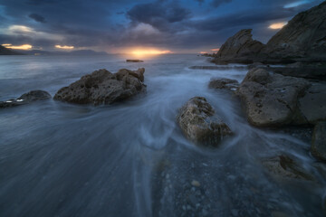 Dramatic seascape at sunset in Azkorri beach, Getxo, Basque Country, with waves flowing between rugged rocks under stormy clouds