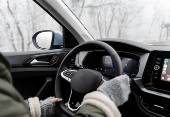 Hands in mittens on the steering wheel, driving a car in winter weather, a trip to the forest