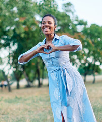 Happy young black woman meditating and daydreaming and relaxing and having fun showing heart shape, love concept,  in nature outdoors