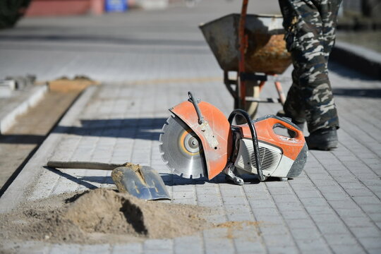Circular saw with shovel, worker pushing cart, pedestrian path construction.