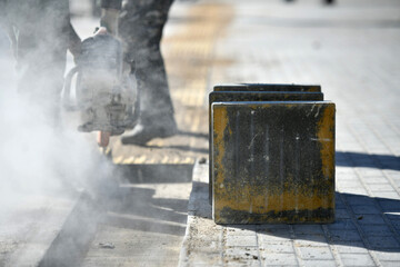 Close-up of concrete block, worker cutting with circular saw, construction work on city street.