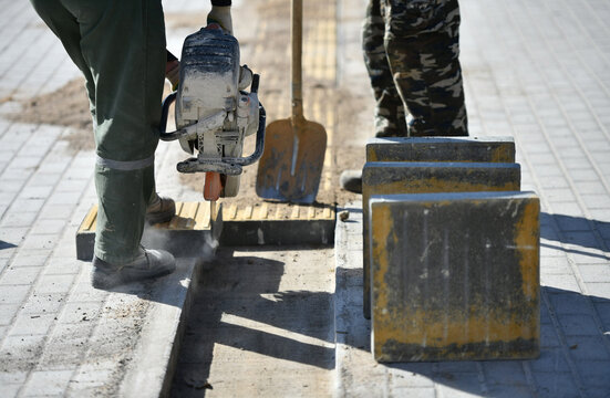 A worker cuts curbstone with a circular saw while building a pedestrian path.