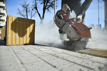 A worker is sawing a road curb with a circular saw, there is a lot of dust.