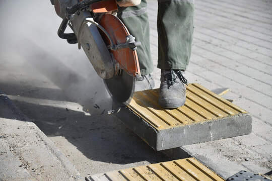 Close-up of worker with circular saw cutting curbstone at construction site.