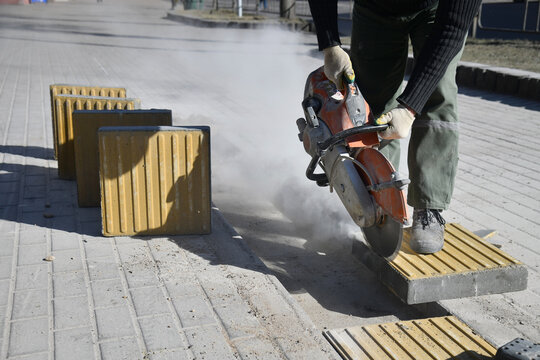 A worker cuts with a circular saw, construction work on a city street.