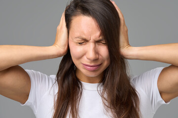 Close-up of woman covering ears tightly with eyes closed in reaction to loud
