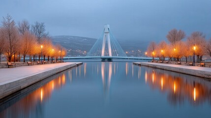 A Twilight View Of A Modern Suspension Bridge Over Calm Water Lined With Illuminated Trees And Snow Covered Ground Under A Cloudy Sky