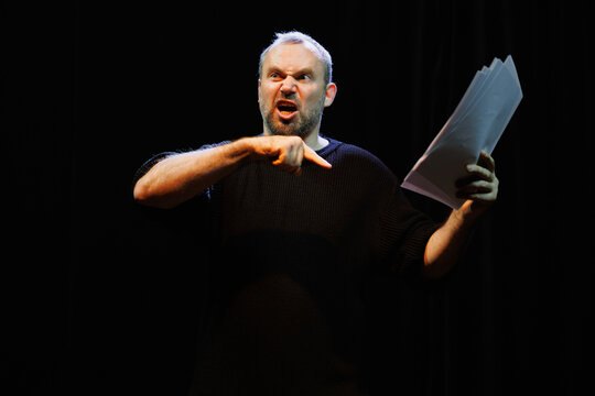 Emotional actor pointing at scenario while playing role of angry man