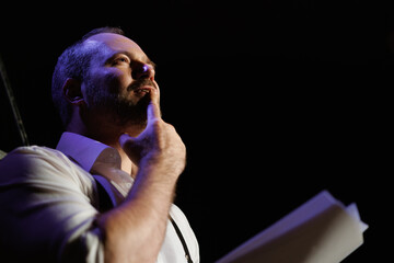 Actor holding scenario and playing role of pensive man in theater
