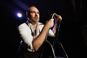 Portrait of adult theater artist performing on ladder on stage 