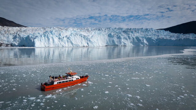 An awe inspiring aerial perspective captures a modern cruise ship gracefully navigating the icy waters in front of the colossal Eqi Glacier in Greenland