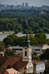 Fototapeta premium Zemun church tower with green roof and view of Belgrade skyline across the Danube River